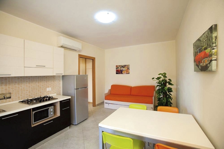Moderne Küche mit Esstisch, bunten Stühlen und Sofa im Hintergrund.