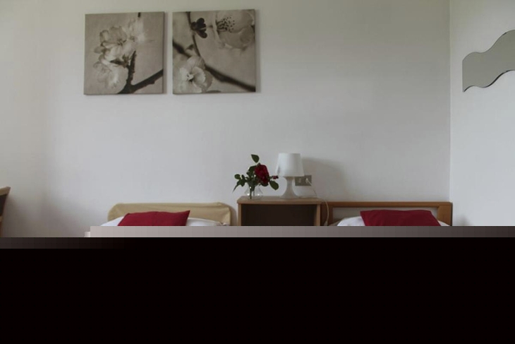 Zwei Einzelbetten mit roter Dekoration in hellem Zimmer.