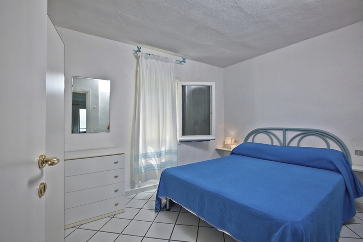Ein einfaches Schlafzimmer mit einem blauen Bett und weißen Möbeln.