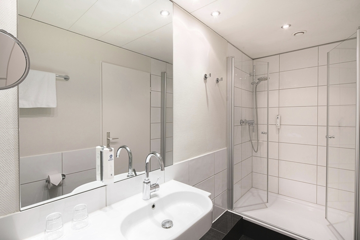 Badezimmer mit großer Dusche, Waschtisch mit Spiegel und weißen Fliesen.