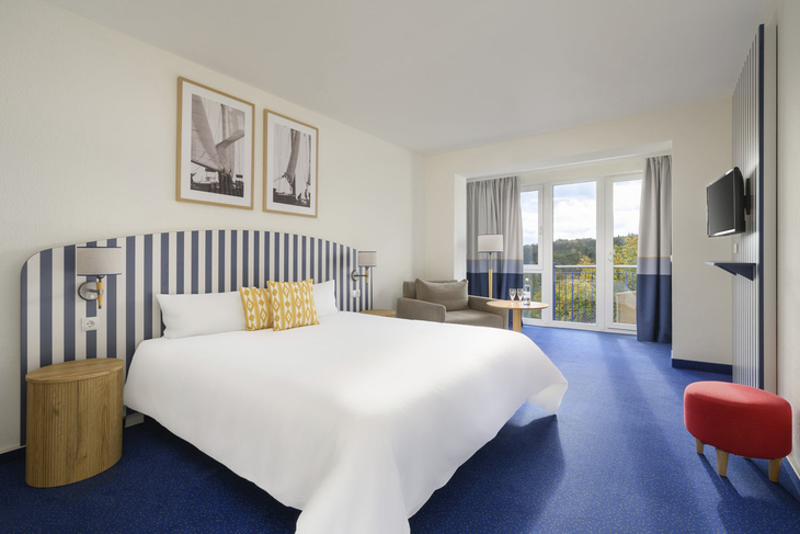 Modernes Hotelzimmer mit Doppelbett, blauen Streifen und großem Fenster.
