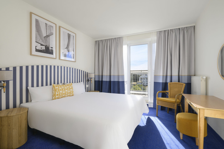 Helles Hotelzimmer mit Doppelbett, blauer Teppich und Balkon in Binz, Rügen.