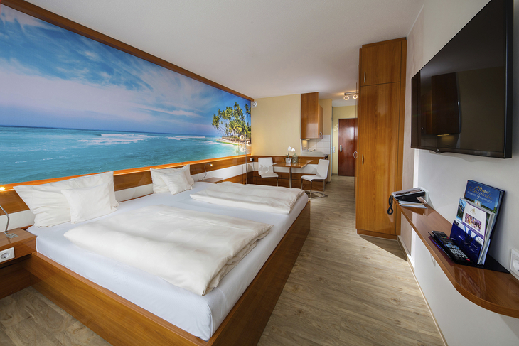 Modernes Gästehaus-Appartement mit Doppelbett, Meer-Wandbild, Holzmöbeln und TV.