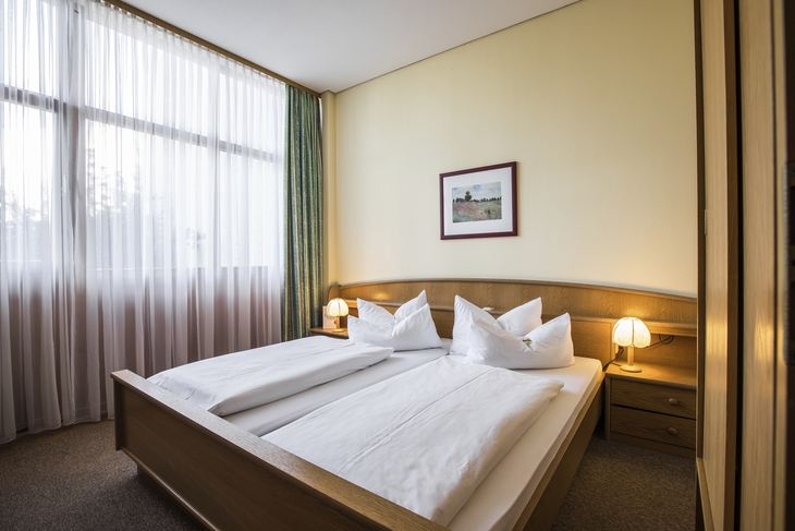 Helles Hotelzimmer mit Doppelbett und großen Fenstern.