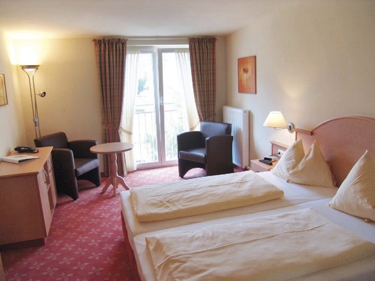 Hotelzimmer mit zwei Betten, Tisch, Stühlen und hellen Vorhängen.