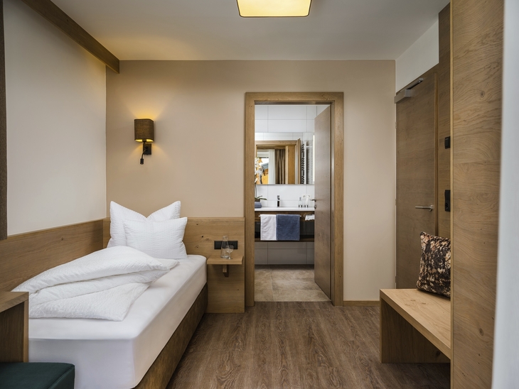 Einzelzimmer im Hotel mit modernen Holzmöbeln und Blick ins Badezimmer.