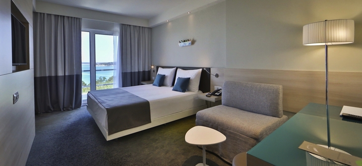 Modernes Hotelzimmer mit Doppelbett, Schreibtisch und großem Fenster mit Meerblick.