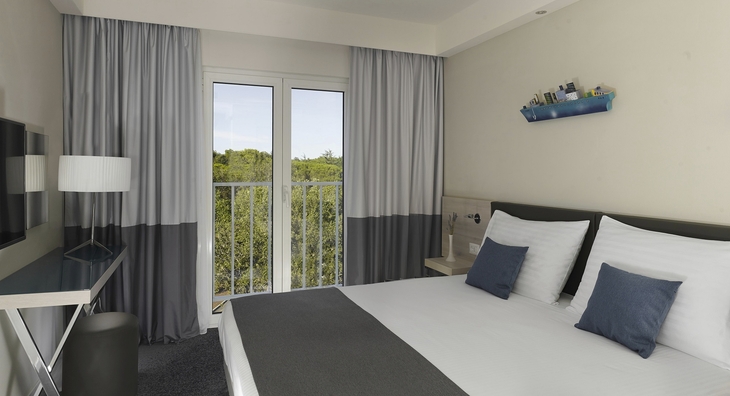 Modernes Hotelzimmer mit Doppelbett, Schreibtisch und großem Fenster mit Vorhängen.