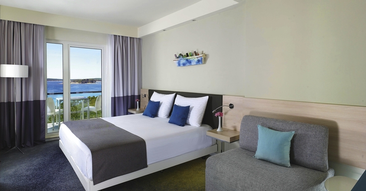 Hotelzimmer mit Doppelbett, Sofa und Blick aufs Meer durch Fenster.