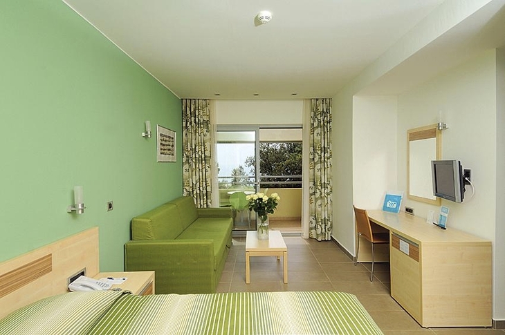 Hotelzimmer mit Doppelbett, Zustellbett, Balkon, Schreibtisch und Fernseher.