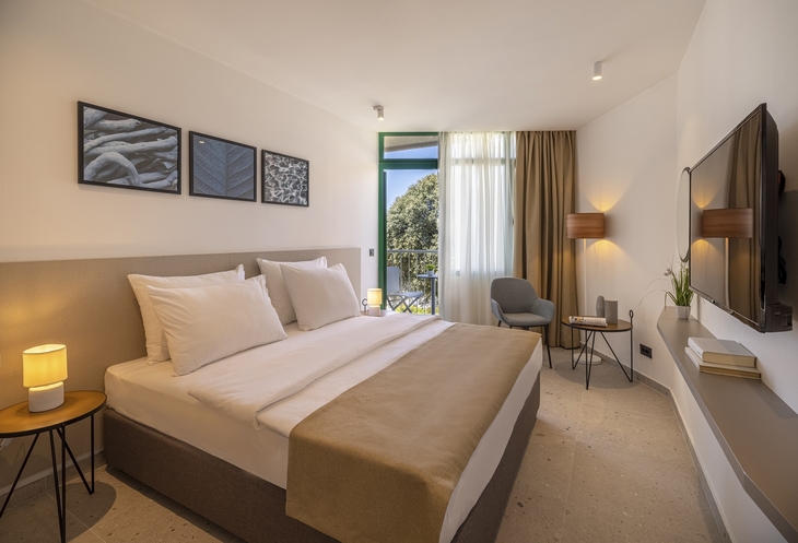 Modernes Hotelzimmer mit Doppelbett, Balkon mit Ausblick, stilvoll eingerichtet.