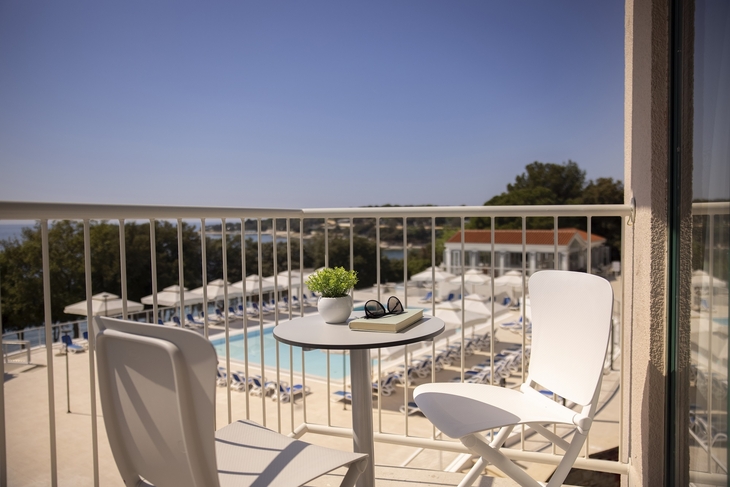 Balkon mit Tisch und Stühlen, Blick auf Pool und Bäume im Resort Funtana.