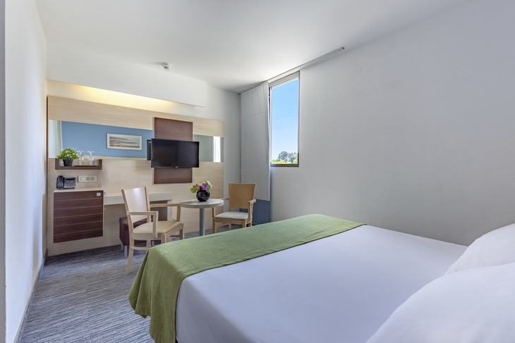 Hotelzimmer mit Doppelbett, Fernseher, Tisch und Blick auf einen Park.