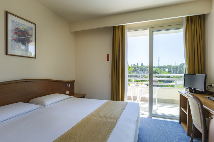 Hotelzimmer mit Doppelbett, Schreibtisch, Balkon und Blick ins Freie.