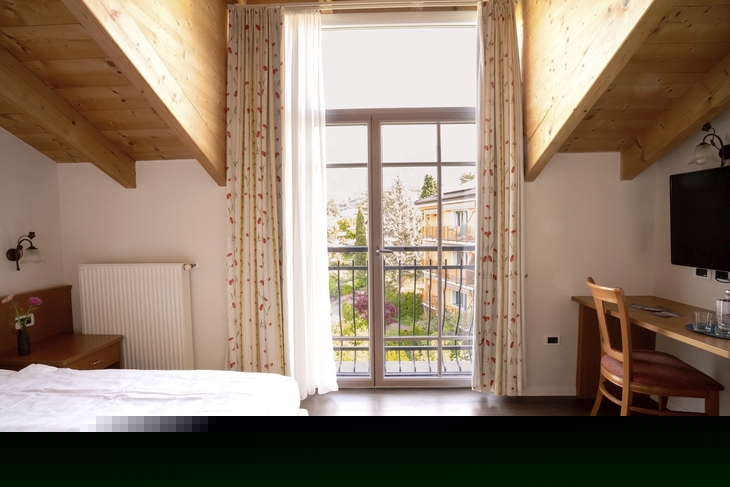 Helles Hotelzimmer mit Holzmöbeln und Balkonblick auf die Umgebung.