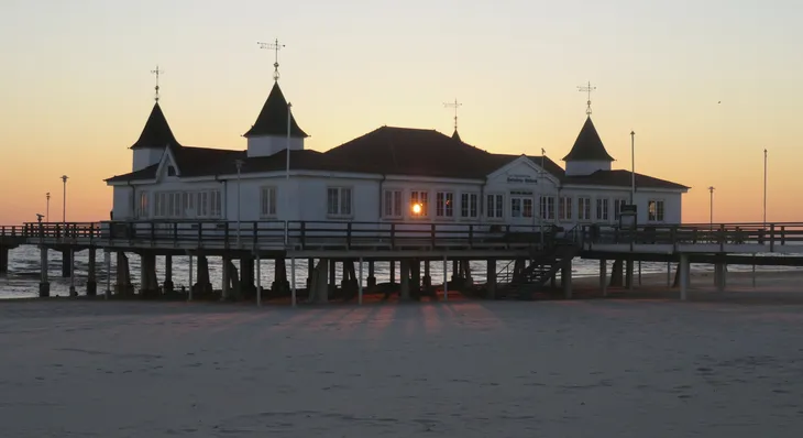 Seebrücke Ahlbeck bei Sonnenuntergang mit beleuchtetem Gebäude und Sandstrand.