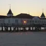 Seebrücke Ahlbeck bei Sonnenuntergang mit beleuchtetem Gebäude und Sandstrand.