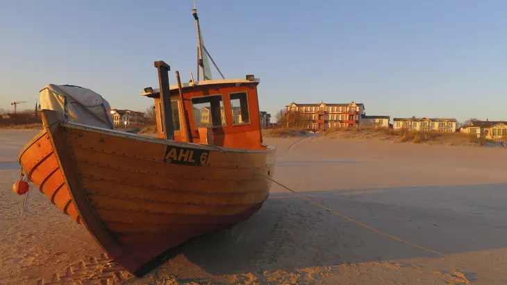 Holzboot am Strand von Ahlbeck bei Sonnenuntergang, Gebäude im Hintergrund.