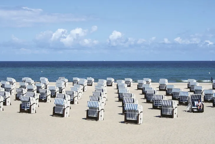 Strandkörbe am Sandstrand mit Blick auf das Meer unter blauem Himmel.