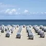 Strandkörbe am Sandstrand mit Blick auf das Meer unter blauem Himmel.