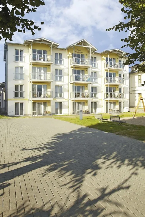 Mehrstöckiges Gebäude mit Balkonen und gepflasterten Hof davor.