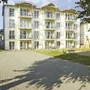 Mehrstöckiges Gebäude mit Balkonen und gepflasterten Hof davor.