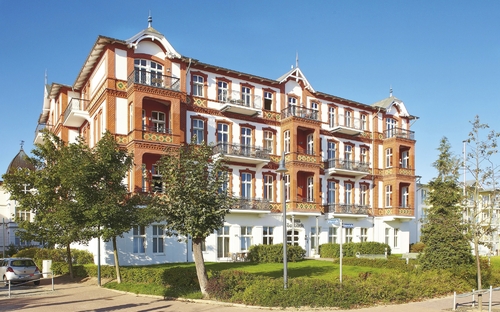Großes, historisches Gebäude mit roter Fassade in Ferienanlage, blauer Himmel.