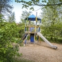 Spielplatz mit Kletterturm und Rutsche im Grünen.