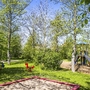 Spielplatz im Grünen mit Rutsche, Schaukelpferd und Bäumen im Sonnenschein.