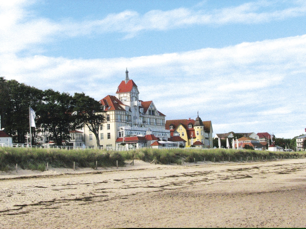 Strand mit Ferienanlage und Bäumen im Hintergrund, blauer Himmel.