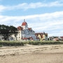 Strand mit Ferienanlage und Bäumen im Hintergrund, blauer Himmel.