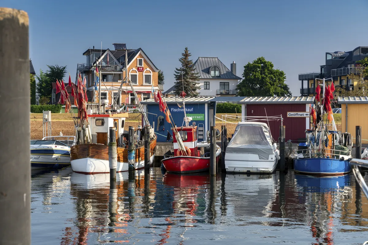 Boote im Hafen von Niendorf vor Gebäuden bei blauem Himmel und sonnigem Wetter.