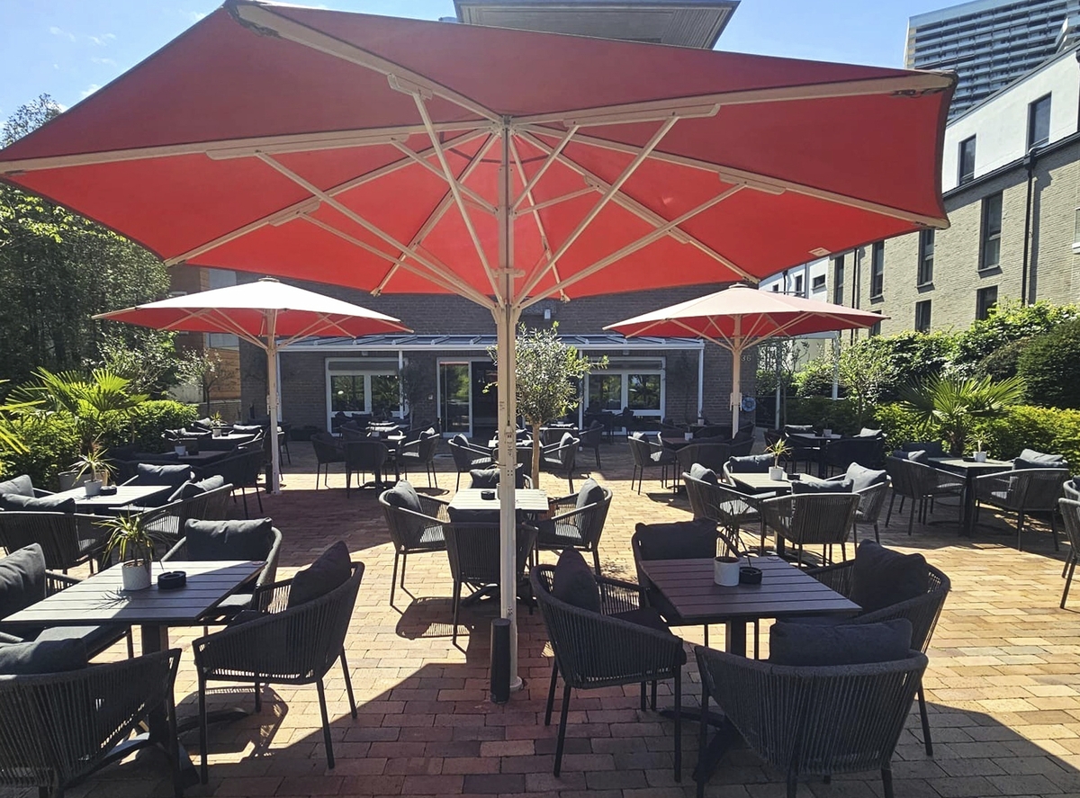 Restaurantterrasse mit roten Sonnenschirmen und leeren Tischen auf gepflasterter Fläche.