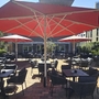 Restaurantterrasse mit roten Sonnenschirmen und leeren Tischen auf gepflasterter Fläche.