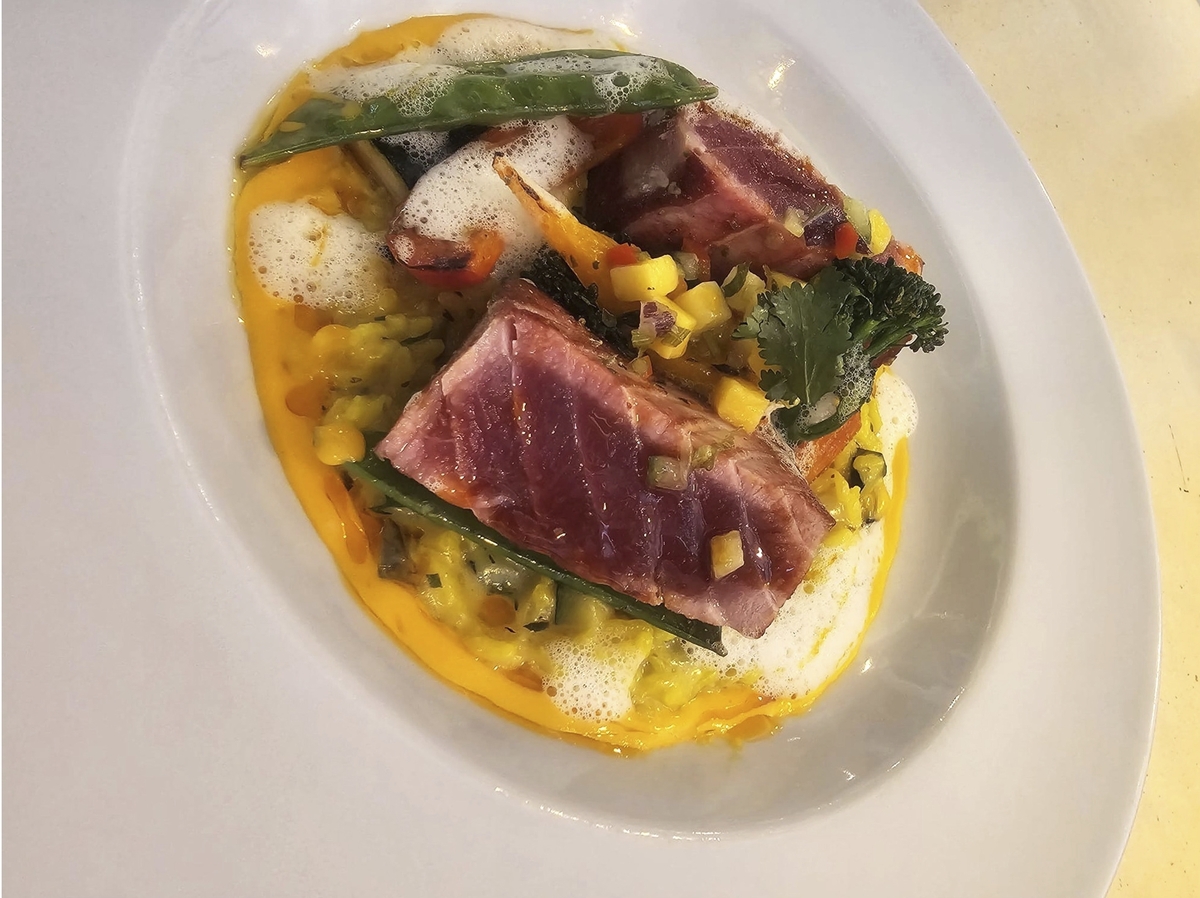 Gourmet-Gericht mit gebratenem Fisch und Gemüse auf weißem Teller.