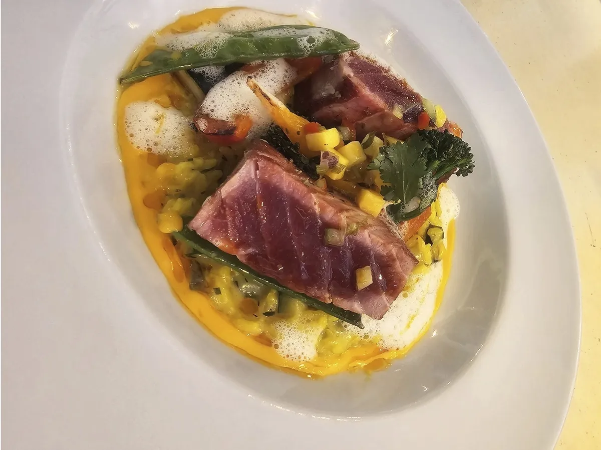 Gourmet-Gericht mit gebratenem Fisch und Gemüse auf weißem Teller.