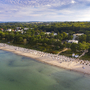 Luftaufnahme von Timmendorfer Strand mit vielen Strandkörben und dahinterliegendem Wald mit Häusern dazwischen, bei leichtbewölktem Himmel.