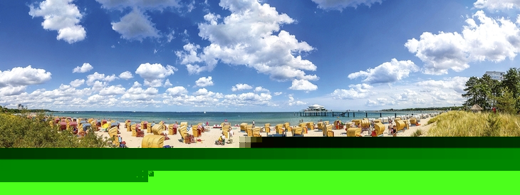 Blick vom Weg zwischen den mit Seegras bewachsenen Dünen auf den Strand mit Strandkörben, dem Meer und blauem Himmel mit Wolken am Timmendorfer Strand.