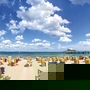Blick vom Weg zwischen den mit Seegras bewachsenen Dünen auf den Strand mit Strandkörben, dem Meer und blauem Himmel mit Wolken am Timmendorfer Strand.