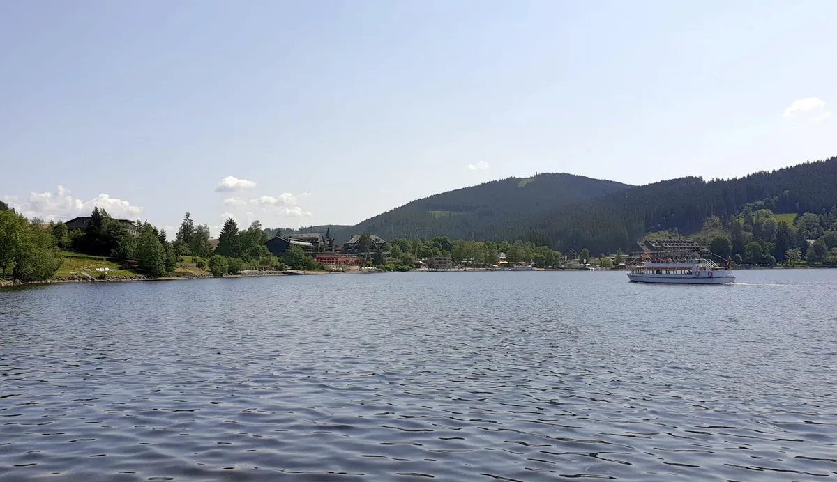 Blick auf den Titisee mit Boot und bewaldeten Hügeln im Hintergrund.