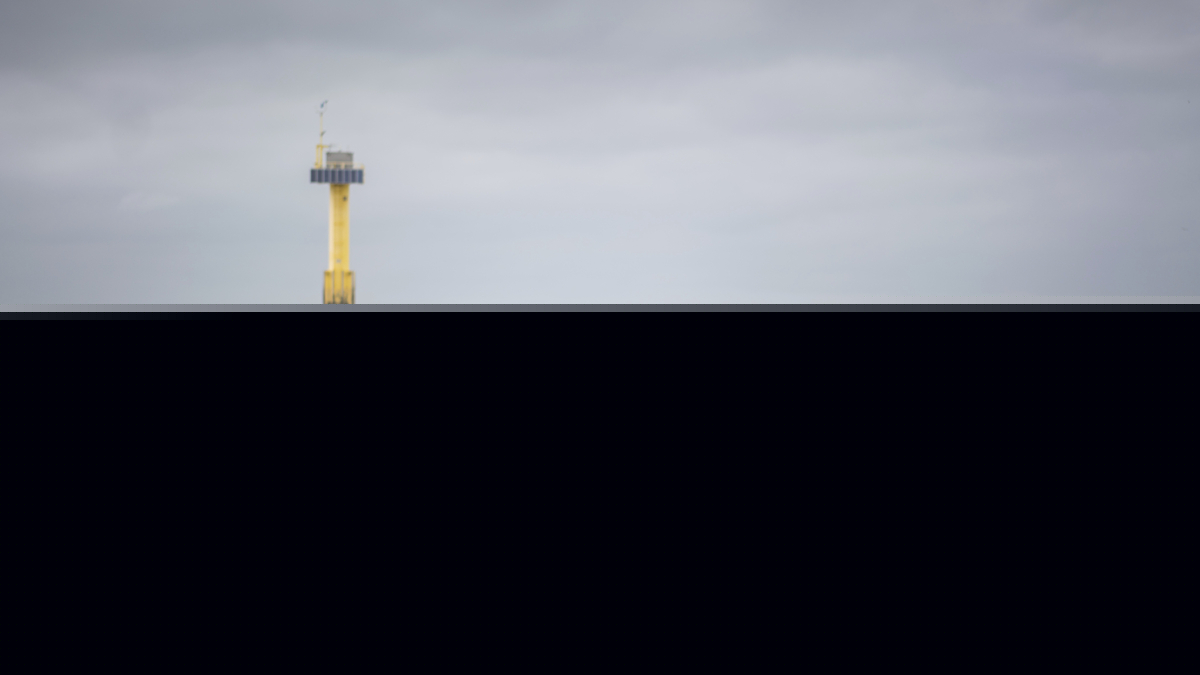 Strand mit Möwen und Leuchtturm im Hintergrund bei bewölktem Himmel.