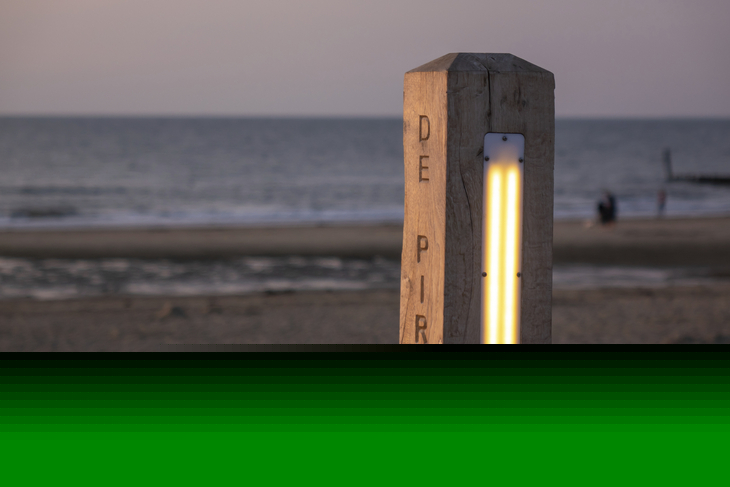 Holzpfosten mit Beleuchtung am Strand bei Sonnenuntergang.