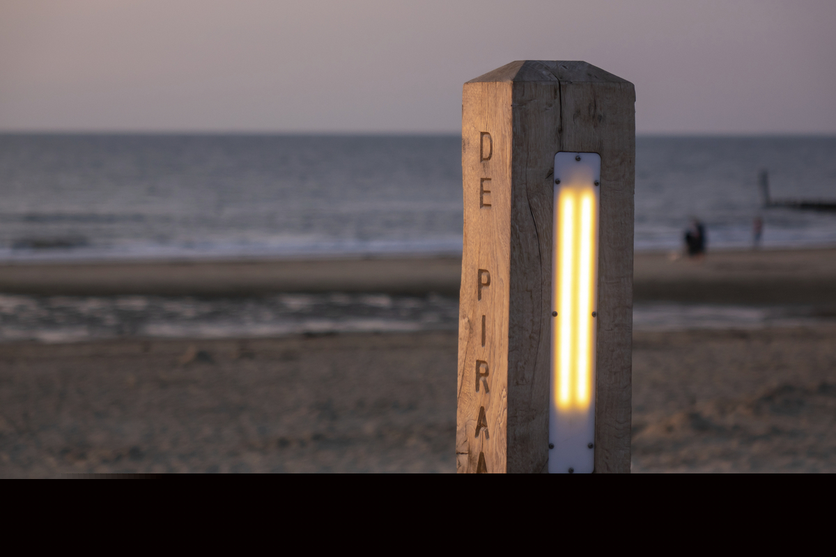Holzpfosten mit Beleuchtung am Strand bei Sonnenuntergang.