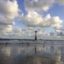 Möwen fliegen über den Strand, Wolken am Himmel, Turm im Hintergrund.