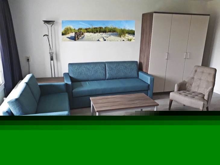 Wohnzimmer einer Ferienanlage mit blauen Sofas, Sessel, Tisch und Schrank.