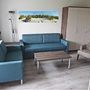 Wohnzimmer einer Ferienanlage mit blauen Sofas, Sessel, Tisch und Schrank.