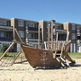 Holzspielplatz in Form eines Piratenschiffs vor Wohngebäude.