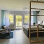 Modernes Einzimmer-Apartment mit Bett, Sesseln, TV und Regalelement, lichtdurchflutet.