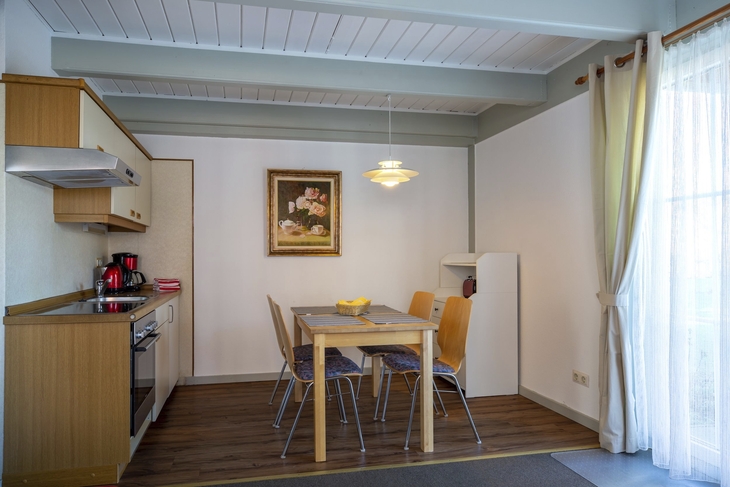 Essbereich mit Holztisch, vier Stühlen, einer Küchenzeile und einem Bild an der Wand.