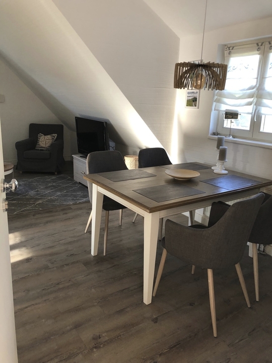 Essbereich in einem hellen Ferienwohnung mit Tisch und Stühlen, Fenster im Hintergrund.